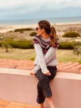 Sweater gris con diseño geométrico en negro y rojo alrededor del cuello, de lana tejido a mano con estilo nórdico.