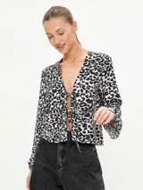 Blusa negra con estampado animal print en blanco y marrón, escote en V con lazo ajustable y mangas largas acampanadas.
