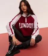 Suéter corto de punto con cuello alto y medio cierre con cremallera. Tiene mangas largas con sisa raglán y lettering "London" en el frente.