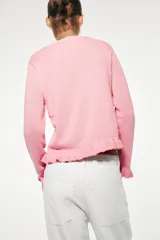 Chaqueta de punto rosa con cuello redondo y manga larga. Detalle de volantes en los bordes y cierre frontal con botones.