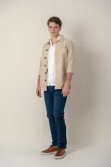 Sobre camisa color beige confeccionada en lino, de corte recto, con cuello clásico, manga larga con puños abotonados, cierre frontal con botones a tono, bolsillo de parche en el pecho y ruedo recto.