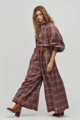 Camisa larga de lino a cuadros color avellana, con cuello camisero clásico, mangas largas abullonadas con puños elásticos, botones de nácar frontales y ruedo curvo, un poco más largo atrás. Incluye cinturón de cuero marrón.