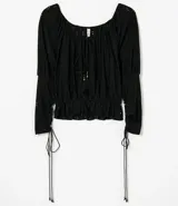 Blusa de poliéster negra con mangas largas abullonadas, escote redondo con botones y bordado en el frente. Tiene volados en el ruedo y ajuste con lazos en los laterales.