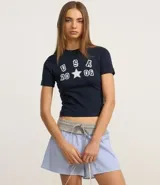 Remera baby look azul marino con estampado frontal de letras "USA" apiladas verticalmente sobre el número "20" y el número "08" separados por una estrella blanca.