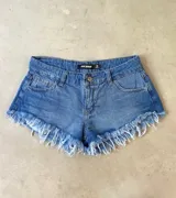 Short de jean de tiro bajo, color azul, con bolsillos delanteros y traseros, y flecos blancos en el ruedo.
