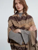 Ruana con mangas color marrón con estampado geométrico en tonos beige y marrón oscuro, con flecos en el borde inferior.