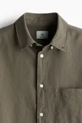 Camisa de algodón Oxford color verde oliva, de corte estándar, con cuello abotonado, tapeta clásica, bolsillo superior abierto, manga larga con puños abotonados y bajo levemente redondeado.