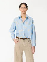 Camisa celeste con estampado floral, confeccionada en poplin con acabado paper touch, acceso mediante cartera oculta con botones y dos bolsillos plaque en el frente.