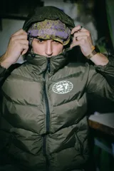 Campera puffer verde oliva con cierre frontal, capucha y logo estampado en el pecho.