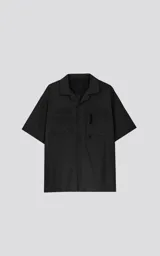 Camisa negra de manga corta estilo técnica, confeccionada en microfibra liviana. Tiene doble bolsillo frontal con cierre de cremallera y broches en lugar de botones.