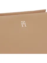 Cartera bandolera pequeña color beige con correa ajustable, confeccionada en poliéster reciclado y poliuretano. Presenta el logo TH metalizado en dorado en la parte delantera.