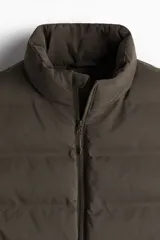 Chaleco puffer color verde oliva, con cuello alto y cierre frontal. Cuenta con bolsillos laterales con cierre y un bolsillo interno con botón a presión.