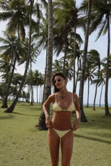 Top de bikini amarillo con textura acanalada, corte triangular, breteles regulables, pieza decorativa de resina verde en el centro y forro interno.