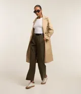 Trench coat largo color beige confeccionado en gabardina de algodón, con cuello solapa, cierre frontal abotonado, cinturón con hebilla, bolsillos laterales y trabillas en los puños.