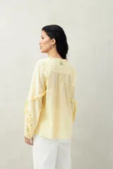 Blusa color amarillo pálido de manga larga con escote en V, mangas abullonadas con volados y botones forrados.