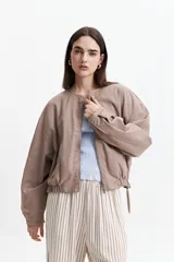 Campera corta color verde militar, sin cuello, con cierre frontal y elástico en la cintura. Tiene bolsillos amplios y mangas largas con puños elásticos.