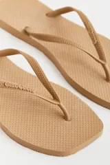 Ojotas color beige con base texturizada y tiras con diseño trenzado y logo de la marca.