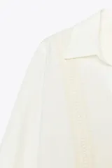 Camisa color crudo confeccionada con lino, de corte recto, cuello solapa con escote pico y manga larga. Presenta aplicación de pasamanería en el frente y cierre frontal con botones forrados a tono.