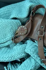 Cartera bandolera marrón de cuero con correa de hombro ajustable, cierre superior con cremallera y detalles de hebillas y aros.