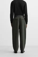 Pantalón relaxed fit color verde oscuro, con pliegues en la parte delantera, bolsillos laterales y traseros de ojal. Cierre frontal con cremallera y botón.