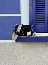 Cartera bandolera negra de nylon con detalles en charol, grifa de goma y cordones combinados. Tiene correa regulable e intercambiable.