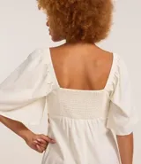 Vestido corto evasê de viscolino color crudo, con escote en V, mangas cortas amplias, recorte cut-out en los laterales de la cintura y volado en el ruedo.