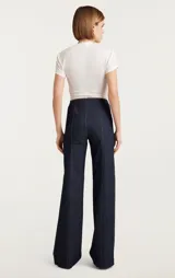 Pantalón acampanado de jean azul oscuro con bolsillos frontales con solapa y cierre frontal con cremallera metálica visible.