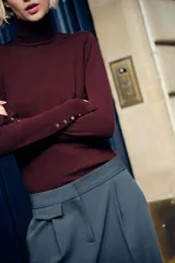Jersey negro de punto liso con cuello alto, manga larga y detalle de botones dorados en los puños.