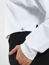Remera blanca de corte cropped, cuello redondo y mangas largas. Presenta logo de la marca en el dobladillo.