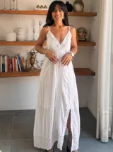 Vestido largo blanco de breteles finos, con escote en V profundo y detalles de encaje y bordados verticales en el frente y en el ruedo. Presenta una abertura lateral en la falda.