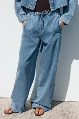 Pantalón de jean azul oscuro, de tiro medio, corte ancho y largo, estilo jogger con cintura elástica ajustable con cordones, bolsillos delanteros de vivo y bolsillos de parche en la espalda.