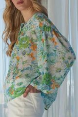 Blusa con estampado floral en tonos verdes y celestes, con cuello con lazo y fruncidos en el pecho.