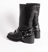 Bota de cuero color marrón oscuro, de caña media, con hebilla y tachas decorativas.