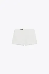 Shorts blancos de tiro bajo con bolsillos delanteros y cierre frontal con cremallera y ganchos metálicos.