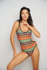 Malla entera con estampado geométrico en tonos naranja, marrón y turquesa, con breteles negros y espalda cavada con tiras cruzadas.