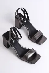 Sandalia de cuero color nude, con tira delgada sobre los dedos, pulsera al tobillo con hebilla y tacón cuadrado.