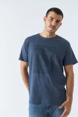 Remera azul de algodón con cuello redondo y estampado frontal con nombres de ciudades: Berlín, Nueva York, Dubai, París y Shanghái.