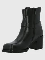Bota corta de cuero color taupe, con caña de 14 cm, taco cuadrado de 6 cm y punta cuadrada. Presenta una correa con hebilla metálica alrededor del tobillo y cierre lateral.