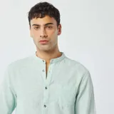 Camisa celeste claro de lino con cuello mao, manga larga con puños abotonados y bolsillo de parche en el pecho.