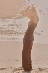 Pantalón marrón de tejido fluido, tiro medio, cintura elástica ajustable con cordones, bolsillos laterales y falsos bolsillos de vivo en la espalda.