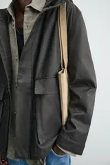 Parka relaxed fit color negro confeccionada en tejido de lino que repele el agua. Tiene cuello con capucha ajustable, mangas largas con puños abotonados, bolsillos frontales con solapa y cierre frontal con cremallera oculta por solapa con botones a presión.