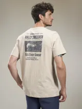Remera de manga corta color beige jaspeado, con cuello redondo. Presenta un estampado gráfico en la espalda con temática de rally, incluyendo texto y una imagen en blanco y negro de un coche de carreras.