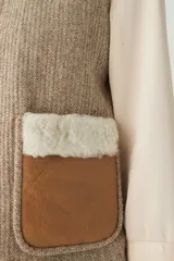 Chaleco corto color beige, de corte recto y abierto, con cuello de piel sintética blanca y apliques de cuero marrón en los bolsillos.