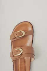 Sandalia plana de cuero color caramelo, estilo 'slide' o 'dos tiras', con hebillas ajustables de metal dorado en cada tira.
