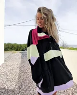 Buzo negro con bloques de color fucsia, verde y lila, con cuello alto con cierre y botones a presión.