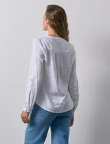 Camisa blanca de lino y rayón, con cuello a la base y escote en V abotonado. Tiene dos bolsillos con botón en el pecho y mangas largas regulables con presilla y botón.