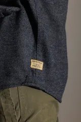 Camisa marrón de manga larga con cuello clásico, cierre con botones y bolsillo en el pecho.