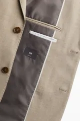 Blazer color beige de corte slim fit, con solapas de muesca finas, botonadura sencilla con cierre de dos botones, bolsillo superior, bolsillos delanteros con solapa, tres bolsillos interiores, botones decorativos en los puños y abertura atrás.