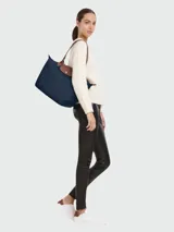 Tote bag de lona en color verde oscuro con detalles en cuero marrón y cierre superior.