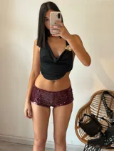 Top negro con escote drapeado, espalda descubierta y detalle de broche dorado en el hombro.